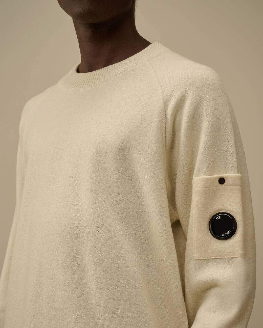 Vista da dietro, modello con maglia girocollo panna taschino con lente taschino C.P. Company da uomo in lana merino